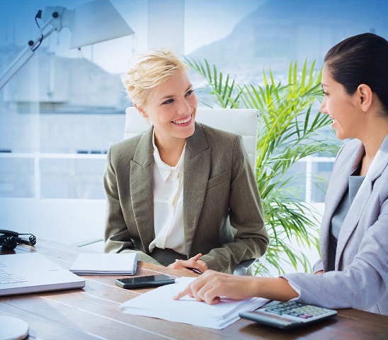 Two businesswomen reviewing documents and financial details at an office desk, representing HR and payroll support services.