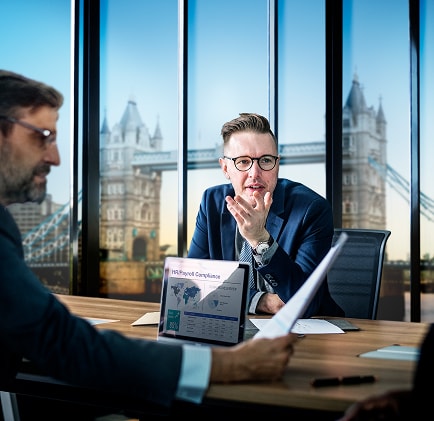 wo business professionals in a modern London office overlooking Tower Bridge reviewing a compliance report, symbolising UK‑specific HR and payroll regulatory support