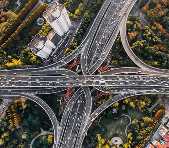 Aerial photograph of a large, multi-level highway interchange surrounded by green and yellow foliage and buildings.